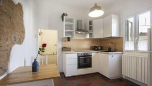 Una cuina petita amb armaris blancs, forn encastrat, un rentapeus i una finestra.
