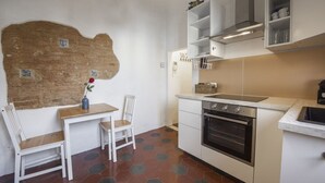 Una cuina amb fogó, forn, armaris blancs i zona de menjador amb caires i taula.