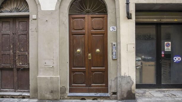 Una porta doble de fusta amb una manilla de bronze, flanquejada per dues portes més petites, i el número '26' sobre la porta principal.