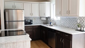 A kitchen with dark wooden cabinets, a stainless steel refrigerator, a black coffee maker, and a white countertop. - Spacious 4BR Home+Patio Retreat (Centennial)