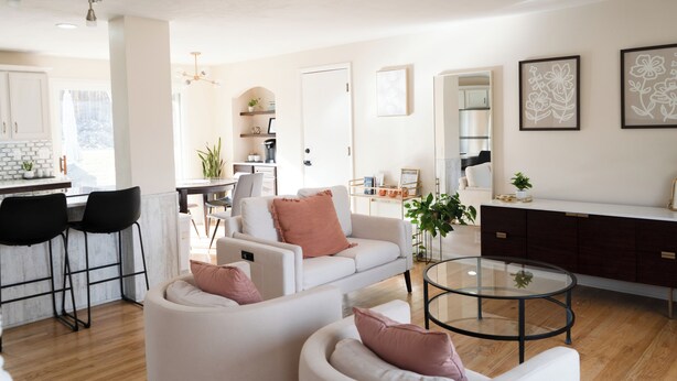 A modern living room with a white sofa, a round glass coffee table, and a dark wooden cabinet. There is a kitchen area with white cabinets and a dining table. - Spacious 4BR Home+Patio Retreat (Centennial)
