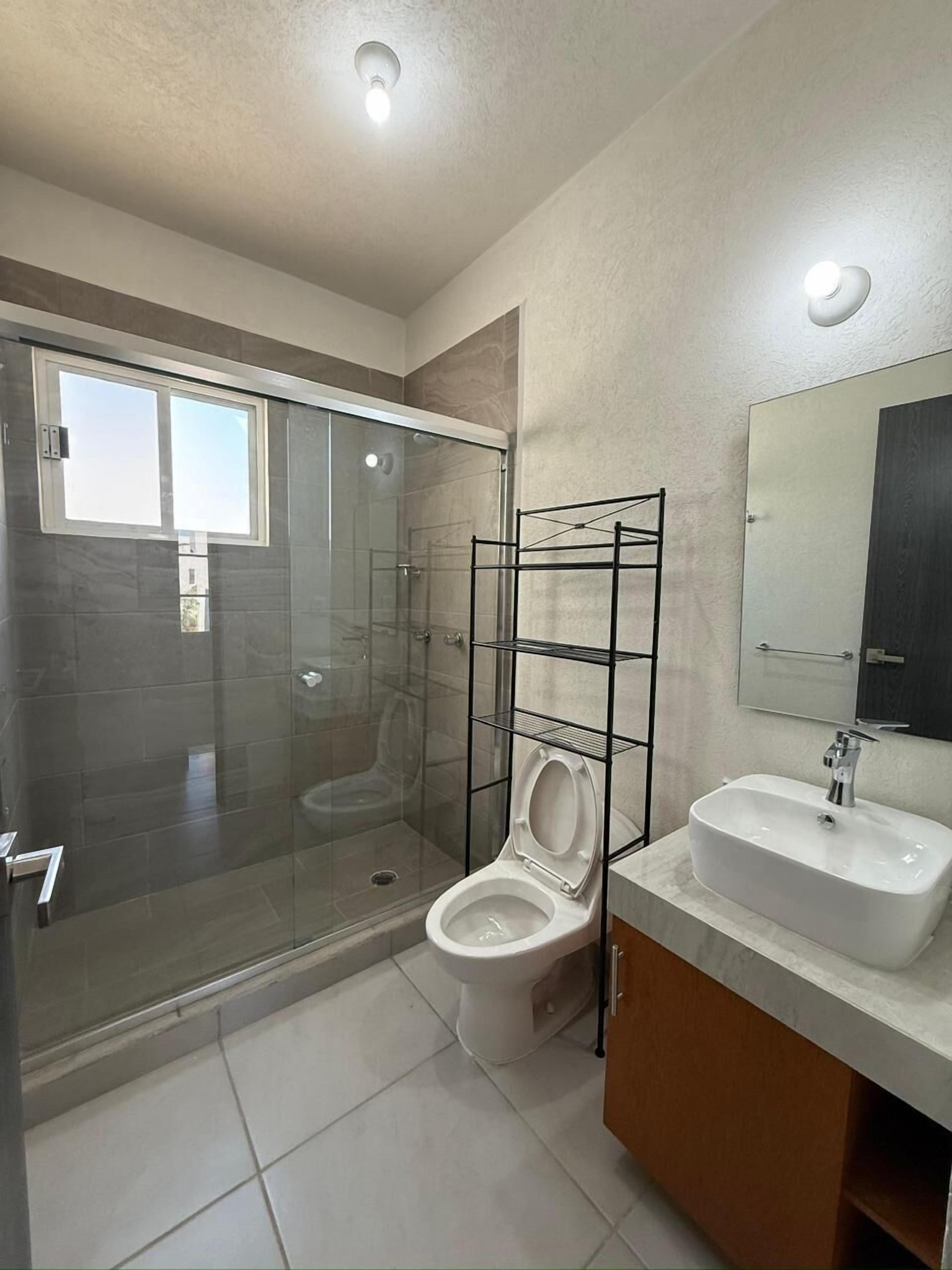A modern bathroom with a glass-enclosed shower, a toilet, and a sink with a mirror above it.