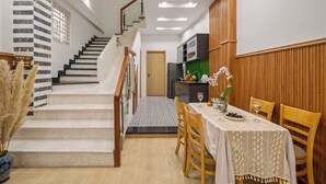A staircase leading to a dining area with a table set for two, a kitchen in the background, and a wooden wall paneling.