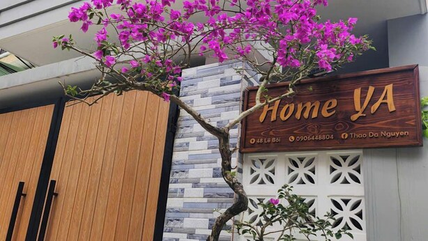 A modern building with a wooden gate, a sign reading 'Home VA', and a tree with purple flowers.