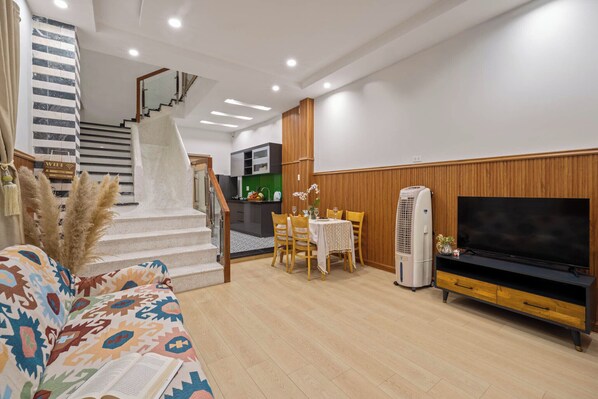 A modern living room with a staircase, a dining area, and a TV stand.