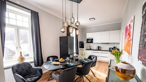 A modern dining area with a black dining table, four black chairs, a chandelier, and a view of the kitchen in the background. - 6 rooms 5 bedrooms 2 bathrooms- close to the city center top renovated (Brunsbüttel)