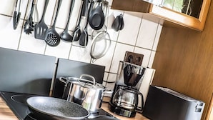 A kitchen with a stove, pots, a coffee maker, and hanging utensils. - Beautiful house with conservatory and garden and large bathrooms (Brunsbüttel)