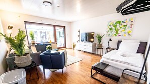 A modern living room with a sofa, a coffee table, a TV, a bed, and a large window. - Beautiful house with conservatory and garden and large bathrooms (Brunsbüttel)