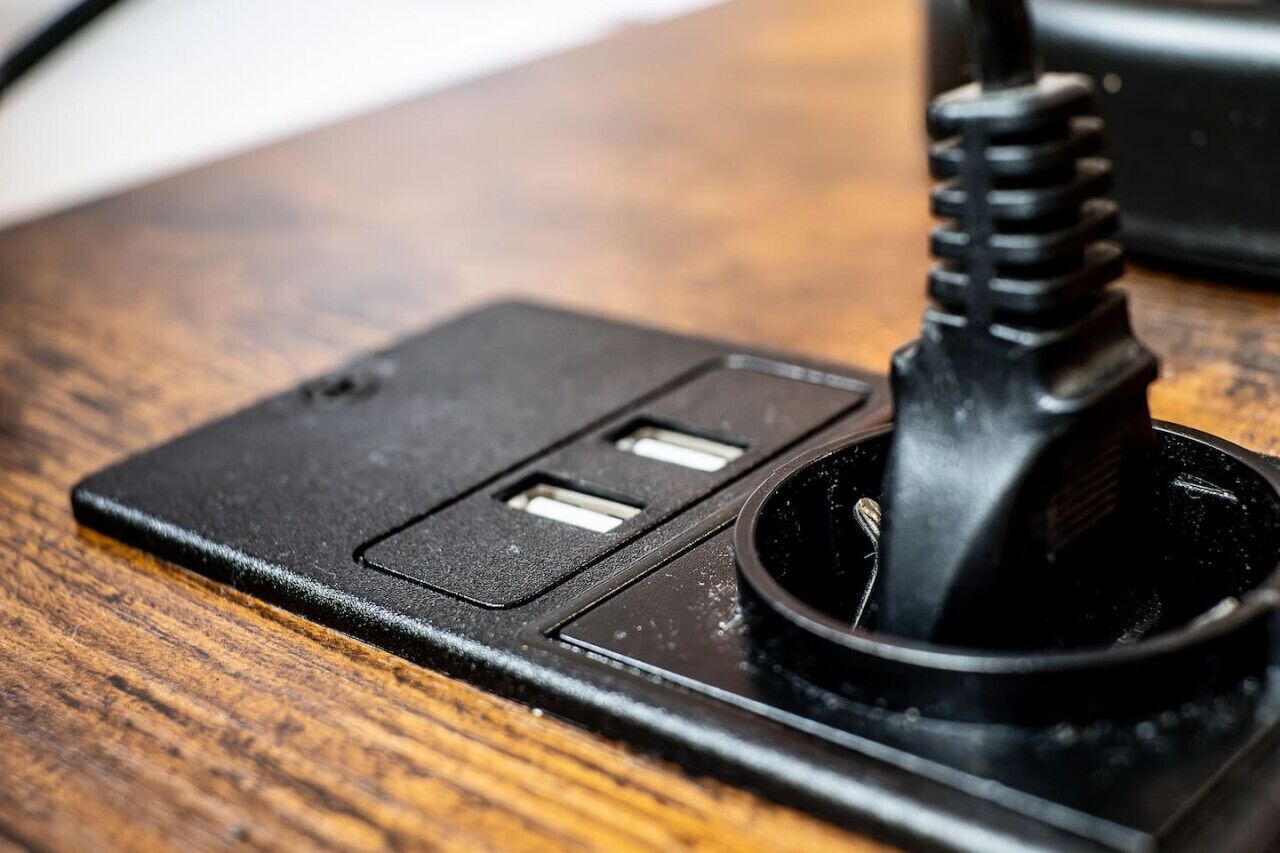 A black power strip with two USB ports and a cable plugged in, placed on a wooden surface.