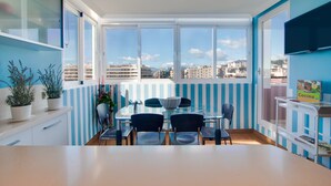 Un coin repas avec une table et des chaises en verre, une vue sur la ville grâce à de grandes fenêtres et un téléviseur fixé au mur.