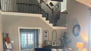 Un salón amplio con un sofá modular grande, un otoman redondo y una escalera que lleva a un nivel superior.