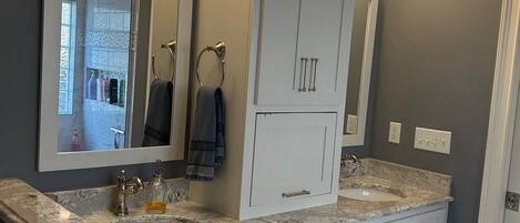 A modern bathroom with a large mirror, two sinks, and a walk-in shower.