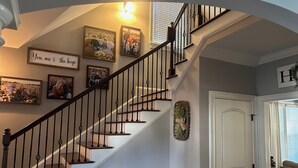 Una escalera con escalones de madera y barandillas negras, flanqueada por fotos familiares enmarcadas y un letrero decorativo.