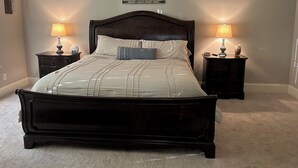Un dormitorio con una cama grande, dos mesitas de noche, una lámpara de pared y un arreglo decorativo.