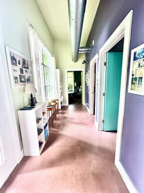 A hallway with a white bookshelf, framed pictures, and a teal door.