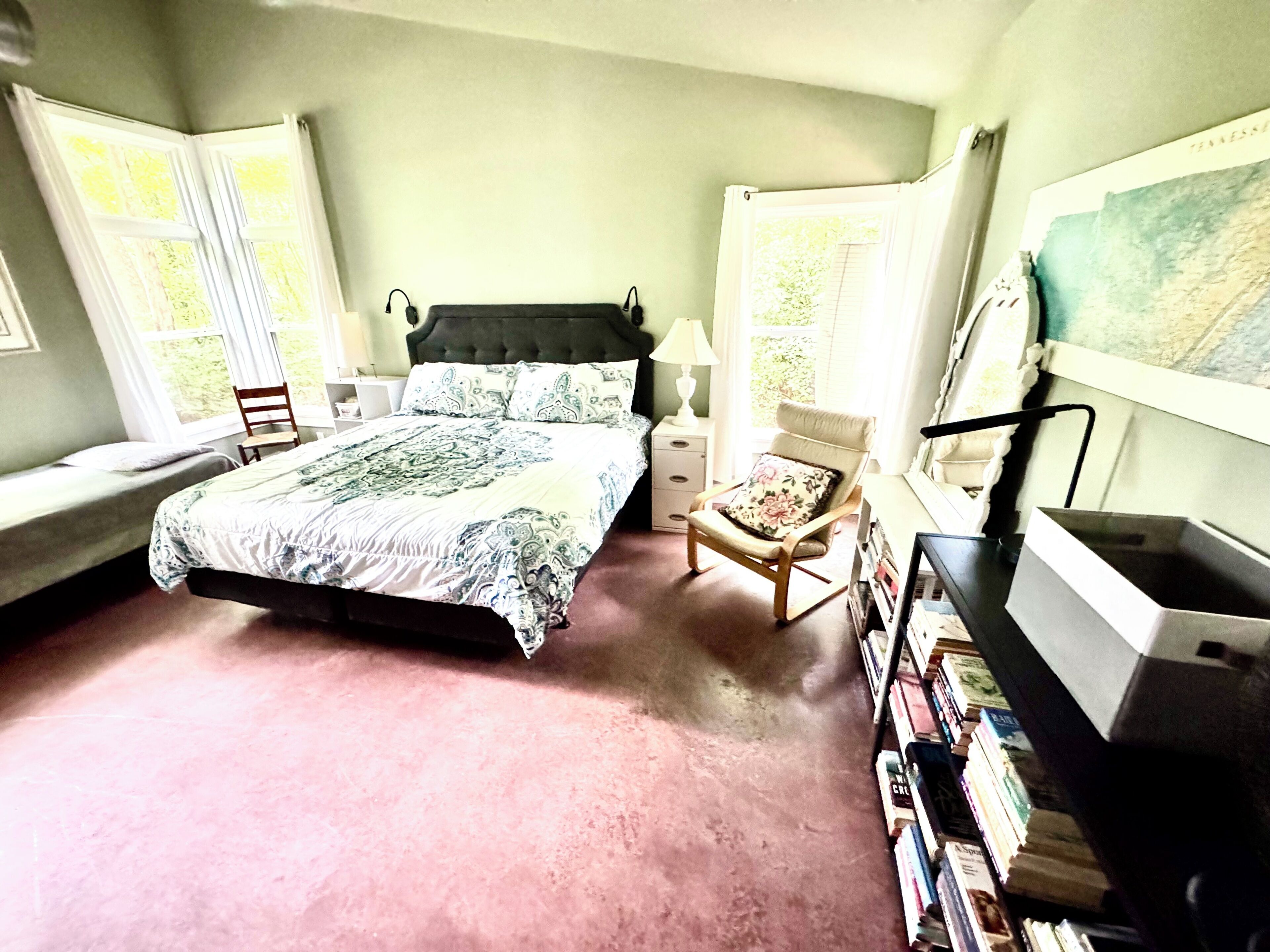 Un dormitorio con cama, una silla, mesita de noche, lámpara y estantería.