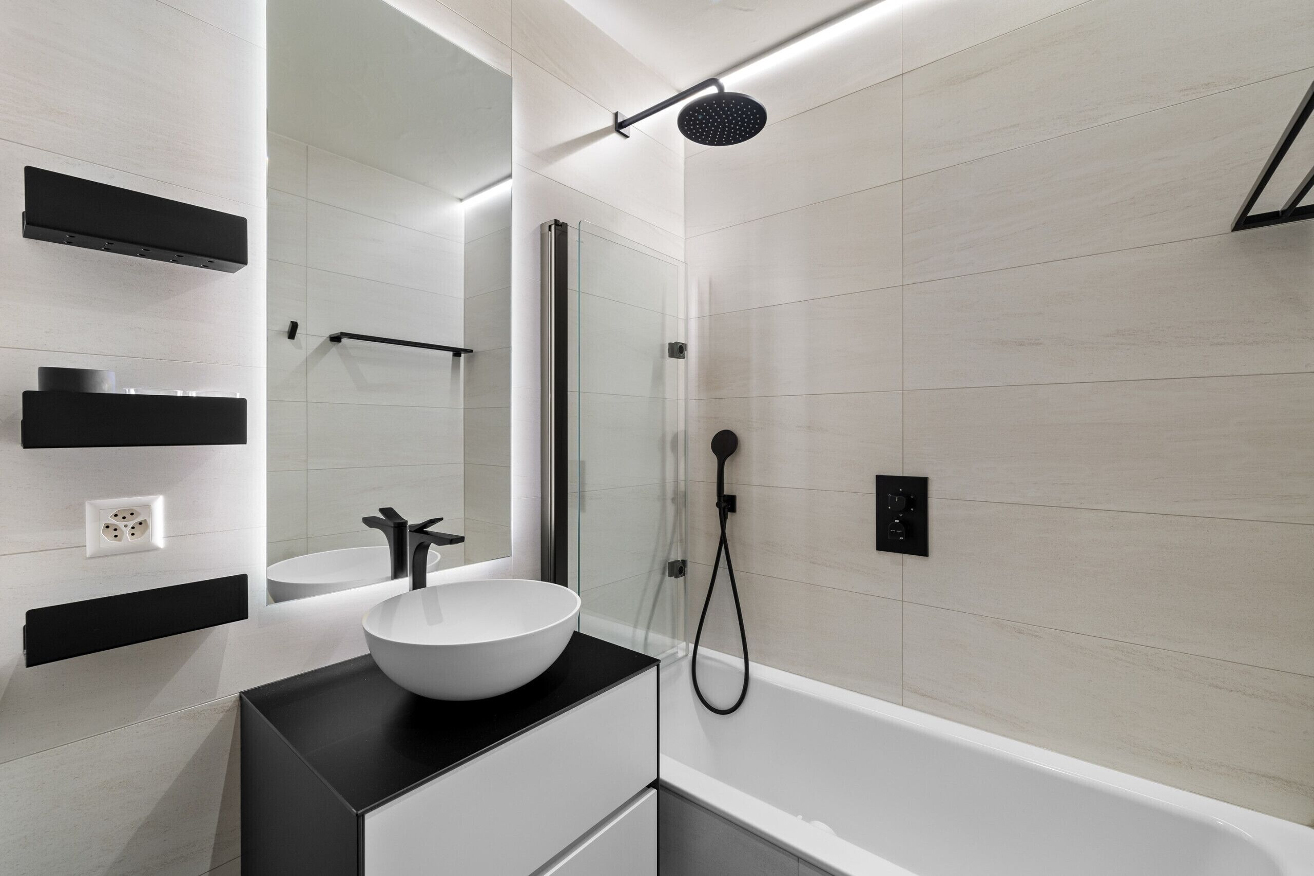 A modern bathroom with a white sink, black countertop, and a glass-enclosed shower area.
