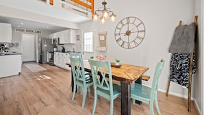 A modern kitchen with white cabinets, a wooden dining table with chairs, a hanging light fixture, and a wall clock. - "High Rock Haven- Fire Pit, Welcome Gifts,  Games room, Hot Tub, 2 lounges, lake (Lexington)