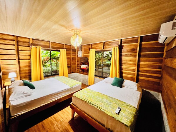A room with two beds, wooden walls, a ceiling light, and a window with curtains.