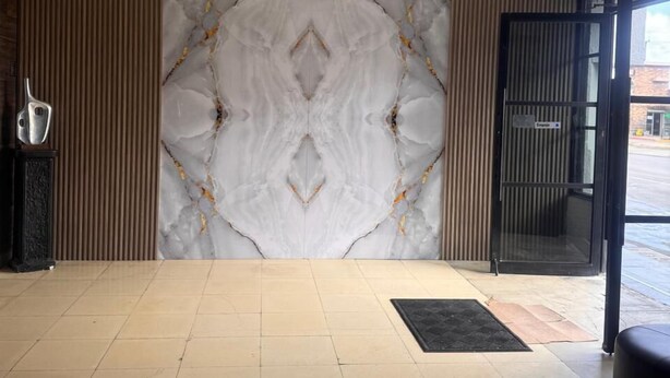 A spacious lobby with a marble wall, a black reception desk, and a glass door leading outside. - Hotel Tj Plaza (Tijuana)
