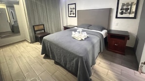 A hotel room with a bed, a nightstand, a wooden cabinet, a mirror, and a ceiling fan. - Hotel Tj Plaza (Tijuana)