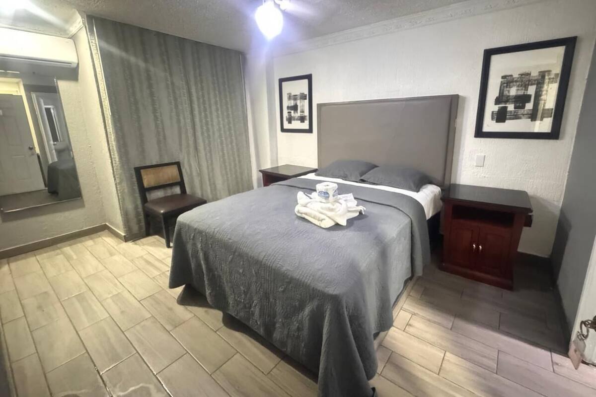 A hotel room with a bed, a nightstand, a wooden cabinet, a mirror, and a ceiling fan.