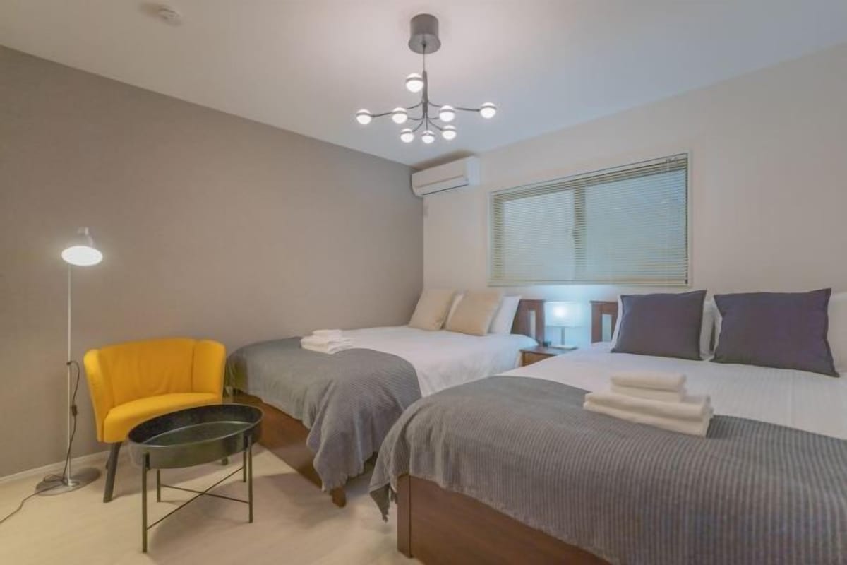 A hotel room with two beds, a chair, a desk, and a lamp.