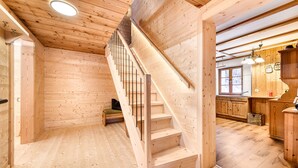 Interior de madera con una escalera, piso de madera y una cocina con armarios de madera y un ventanal.