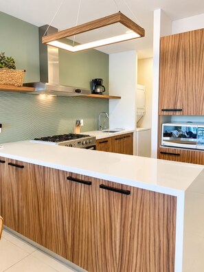 Una cocina moderna con una isla central, armarios de madera, horno empotrado y una lámpara colgante.