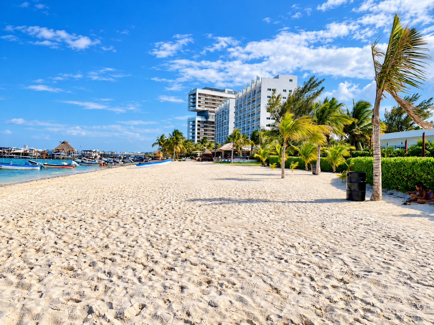 A beach with a hotel in the background, palm trees, and boats.