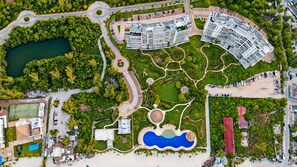 Eine Vogelperspektive zeigt einen Urlaubsort mit mehreren Gebäuden, einem großen Pool im Zentrum und umliegender Bepflanzung.