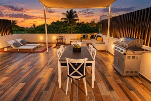 An outdoor patio with a dining table, chairs, a grill, and lounge chairs.