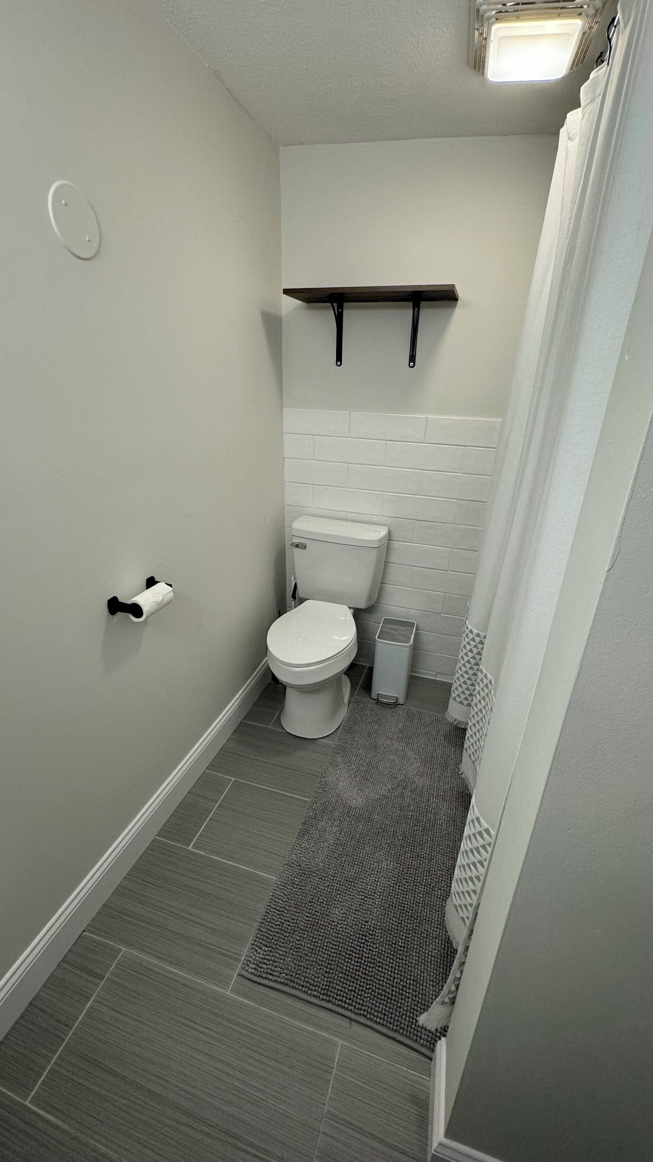 A small bathroom with a toilet, a trash can, a towel rack, and a shower curtain.