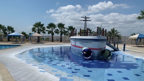 Ein schwimmender Pool in Bootsform, umgeben von Palmen und überdachten Sitzbereichen.