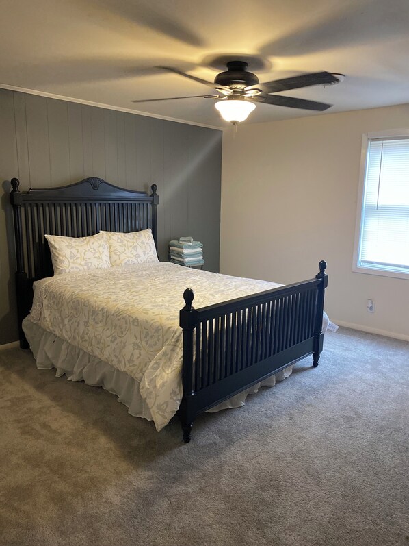 A bedroom with a dark wooden bed, a ceiling fan, and a window with blinds.