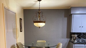 A dining area with a glass table and four chairs, a hanging light fixture, and a kitchen with cabinets and a mixer. - Spacious 5-bedroom house in fabulous Hot Springs 1.2 miles from Oaklawn Park (Hot Springs)