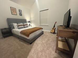Een slaapkamer met een bed, een bureau, een gitaar en een raam.