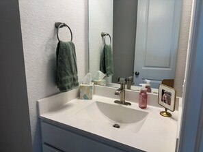 Een badkamer met een wit wastafel, een spiegel, een handdoekhouder, een zakdoekendoos en twee flessen zeep.