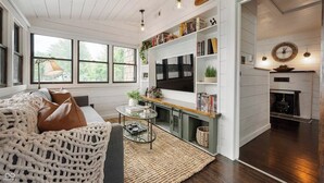 A cozy living room with a large window, a fireplace, and a bookshelf filled with books.