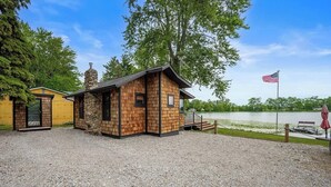A small cabin with a stone chimney, wooden siding, and a dock extending into a lake.