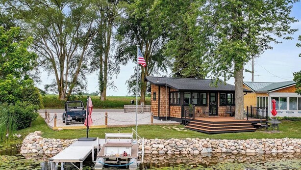 A lakeside cabin with a dock, a covered outdoor seating area, and a flagpole.