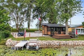 Un chalet au bord du lac, doté d’un quai, d’un espace extérieur couvert avec des sièges et d’un mât pour drapeau.