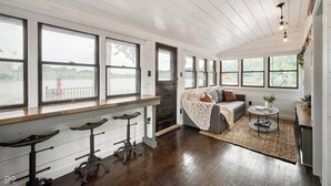 A spacious room with large windows, a cozy seating area with a sofa and cushions, a small round table, and a bar area with stools.