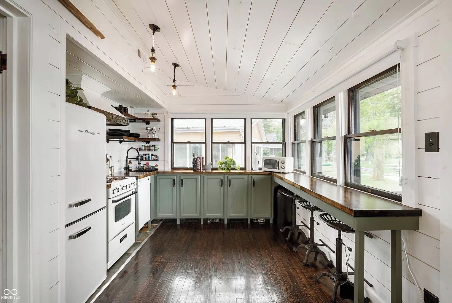 Une cuisine avec des meubles blancs, un plan de travail en bois et une fenêtre donnant sur un jardin.
