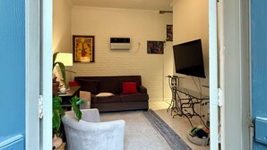 Een woonkamer met een bank, een witte fauteuil, een televisie en een plafondlamp.