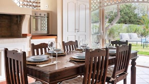 A dining area with a wooden table set for six, a brick oven, and a white door.
