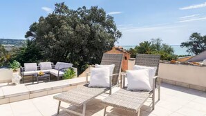 A terrace with wicker lounge chairs and a sofa, overlooking a scenic view.
