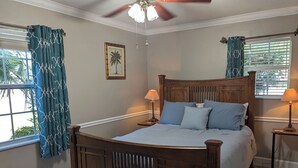 A bedroom with a wooden bed, two bedside tables with lamps, a ceiling fan, and a window with curtains.