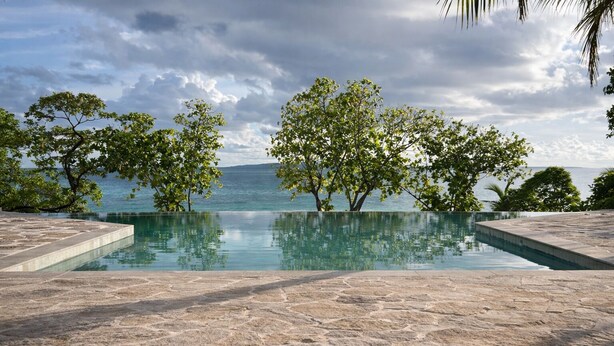 Una piscina de piedra con vista al mar y a los árboles.