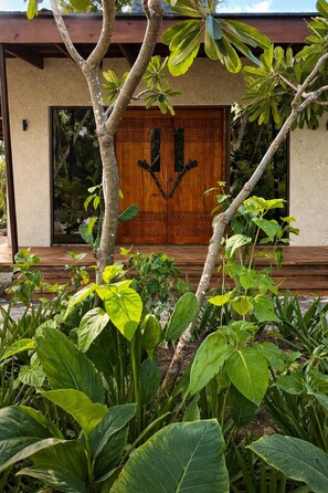 A wooden door with a decorative design, surrounded by lush green plants. - Serenity Sands Island Glamping (Kadavulailai Island)